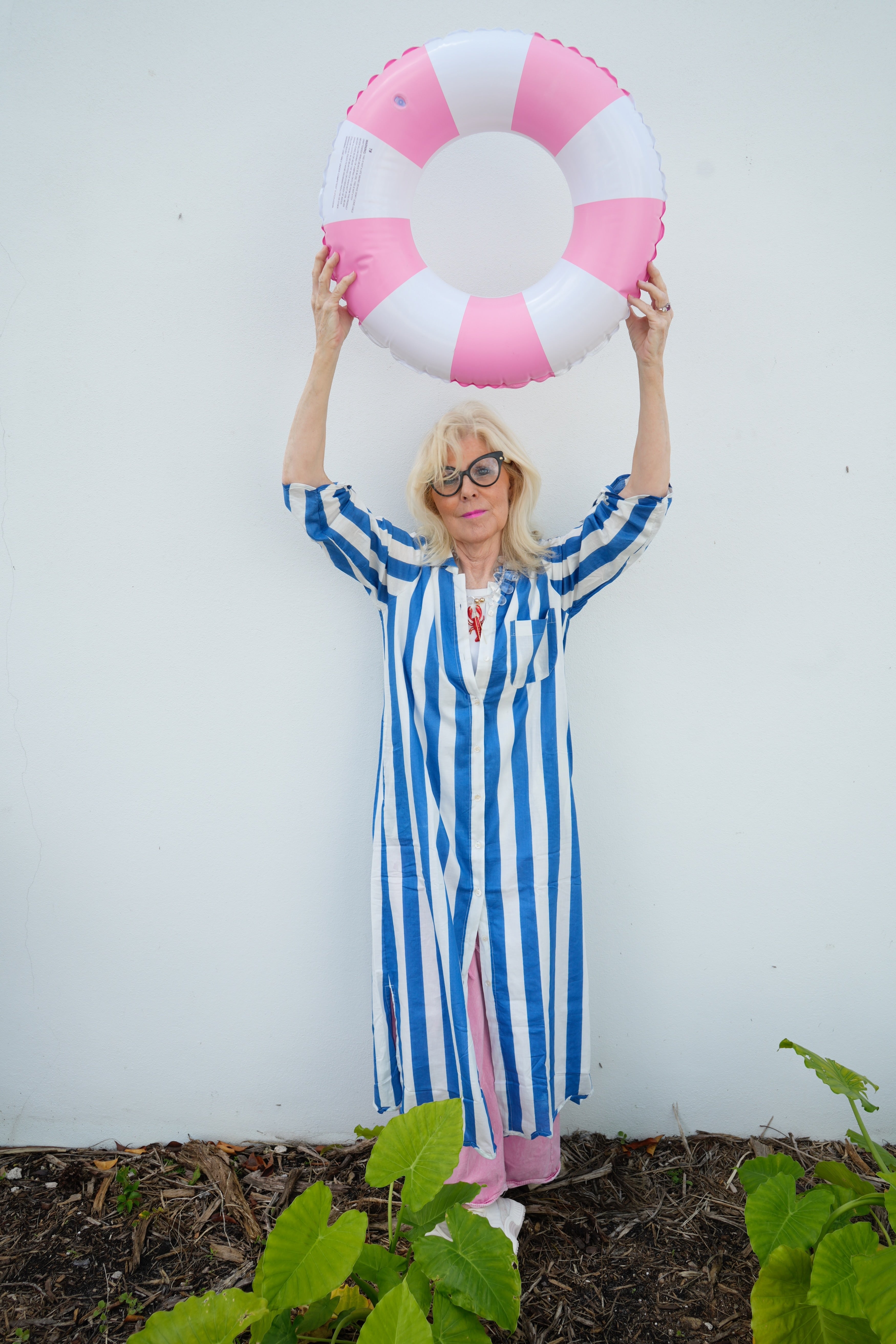 Person in a blue and white striped dress holding a pink and white life buoy against a white background.
