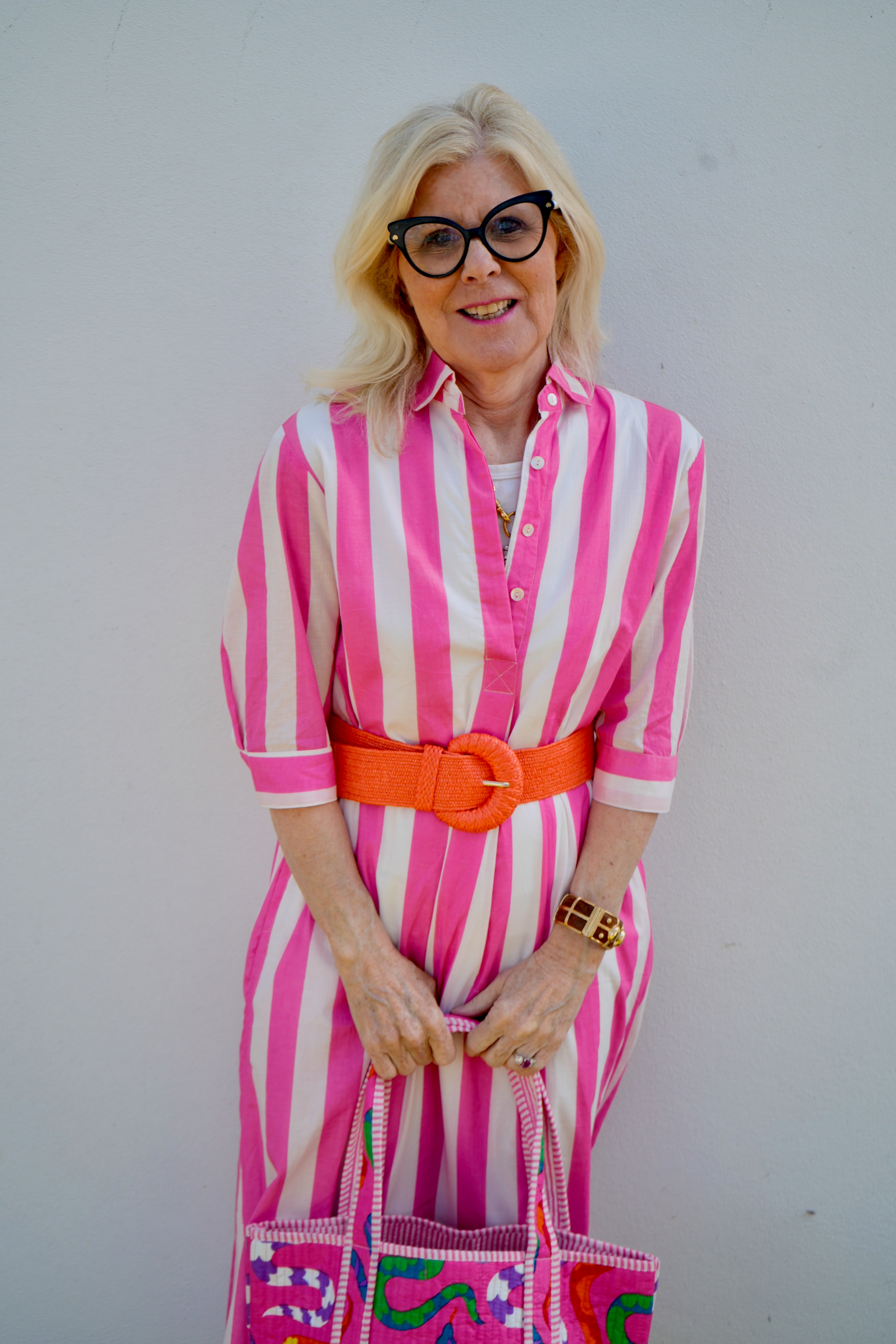 Woman wearing a pink and white striped dress with an orange belt against a plain background