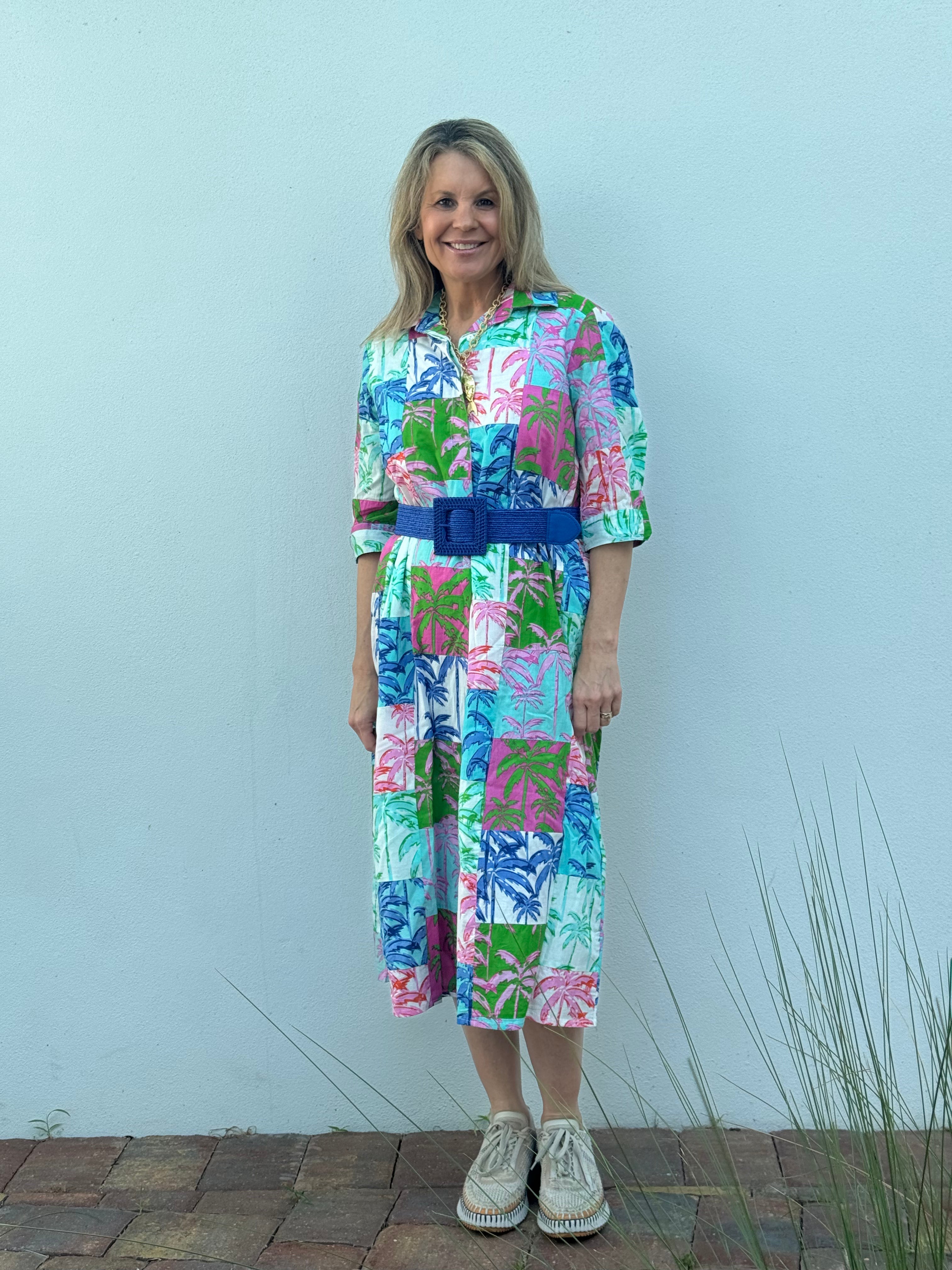 Woman wearing a colorful dress with a blue belt against a light gray background