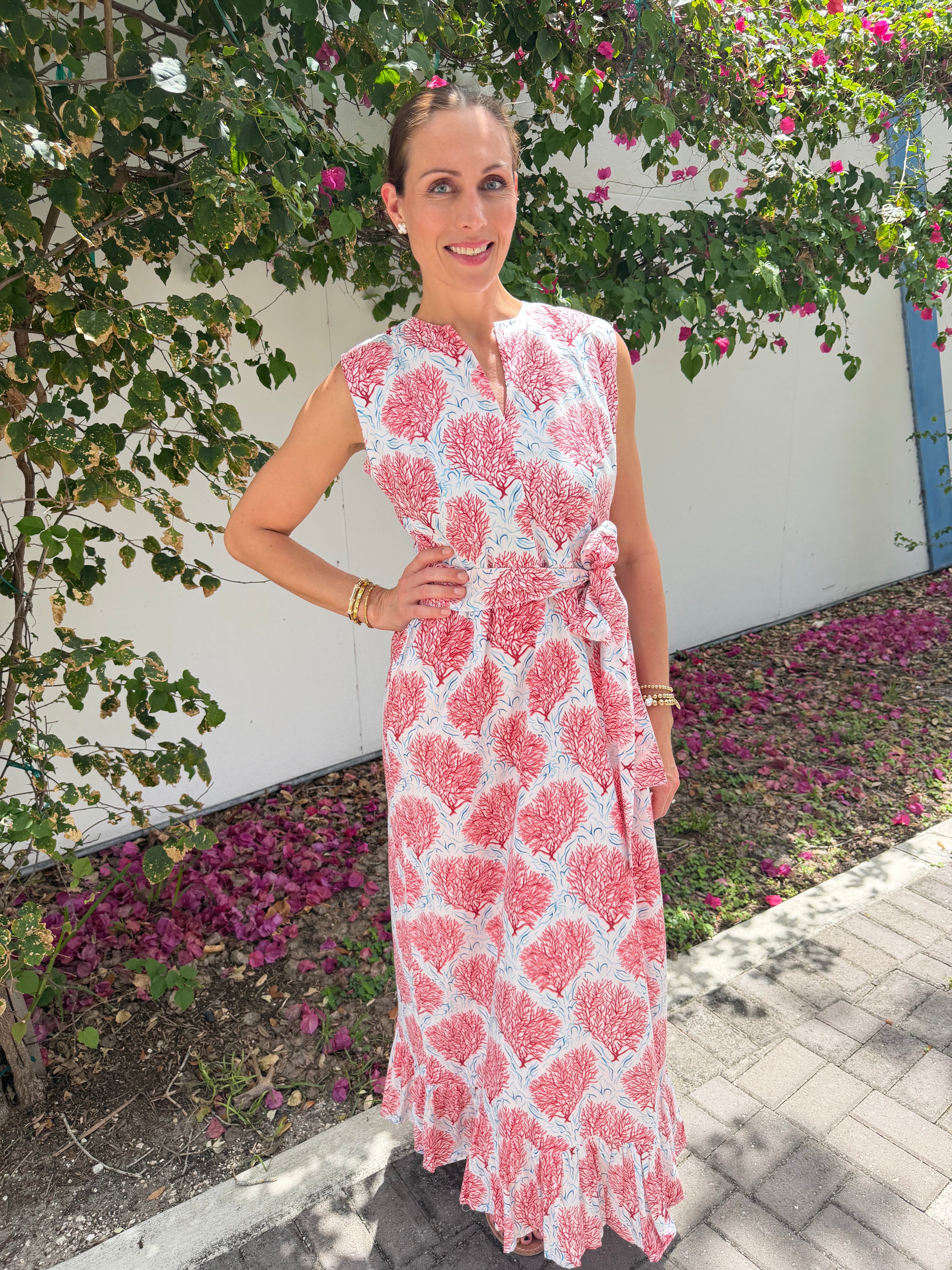 Woman wearing a pink and white patterned dress standing in a garden with flowers.