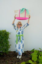 Woman holding a colorful bag above her head with a white background and greenery at the base.