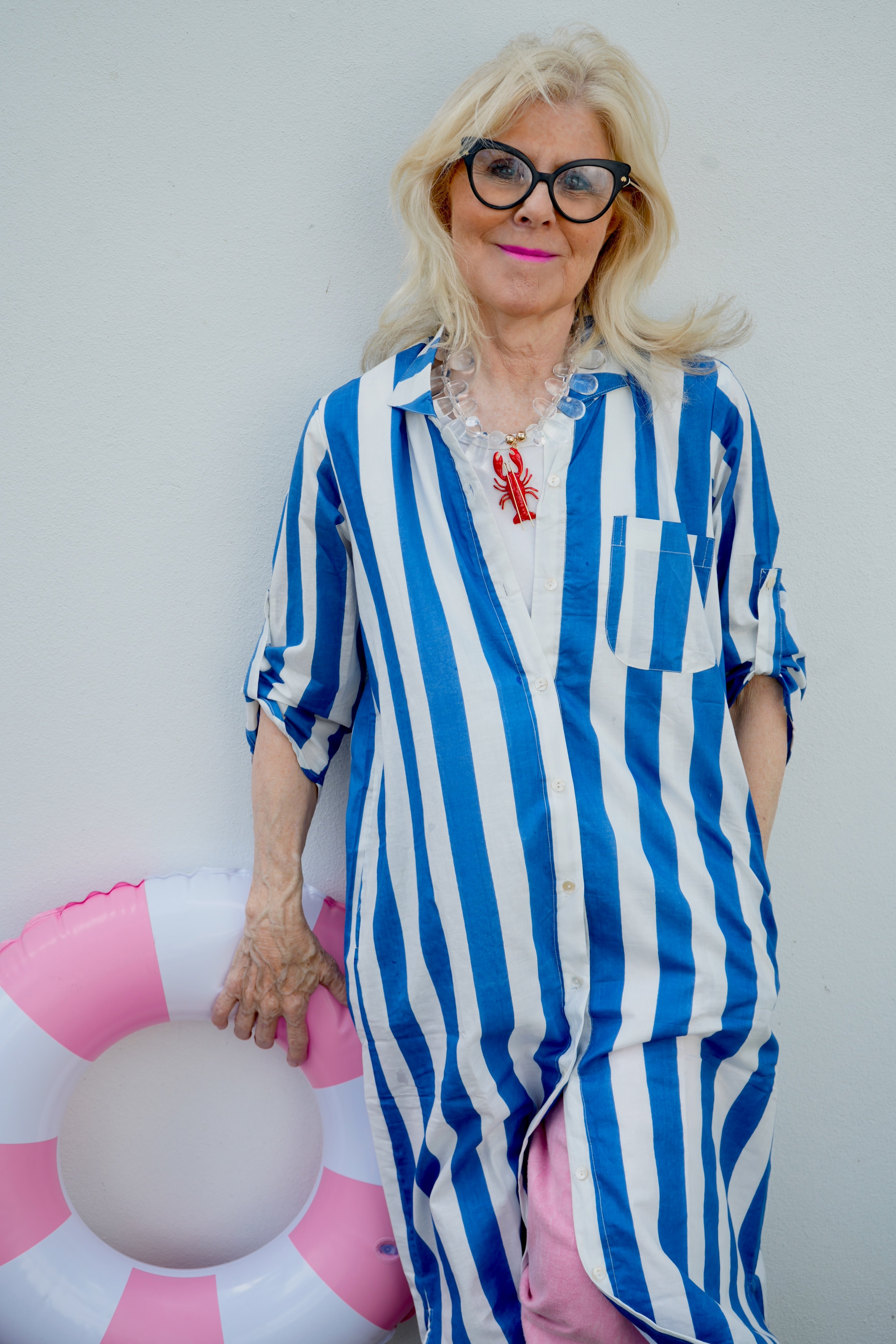 Woman in blue and white striped outfit holding a pink inflatable ring against a plain background