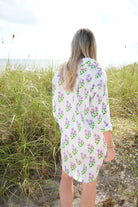 Woman wearing a floral dress standing on a beach with grass and sand.