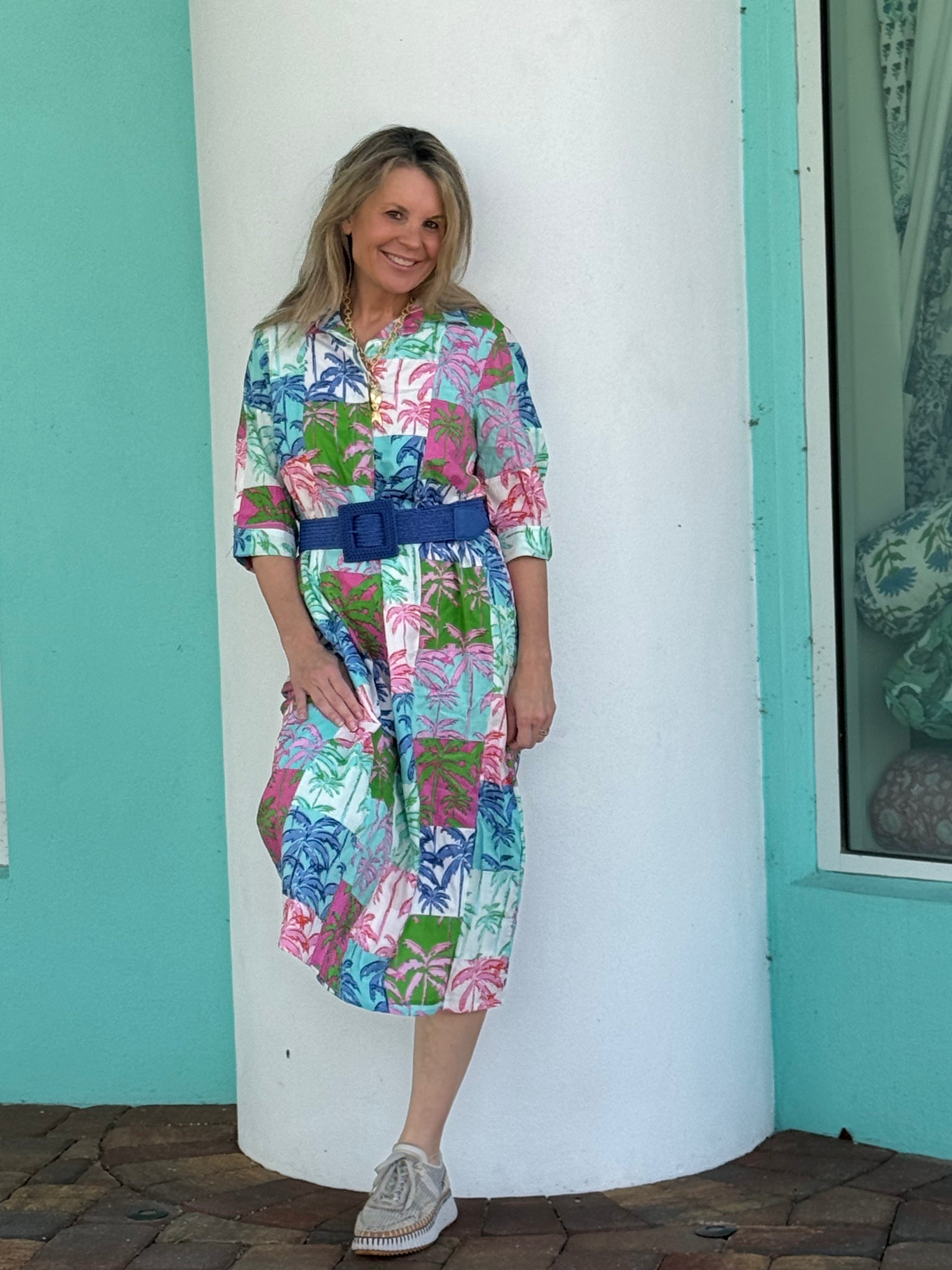 Woman wearing a colorful patterned dress with a blue belt against a light blue wall.