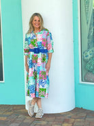 Woman wearing a colorful dress with a blue belt standing in front of a turquoise wall.