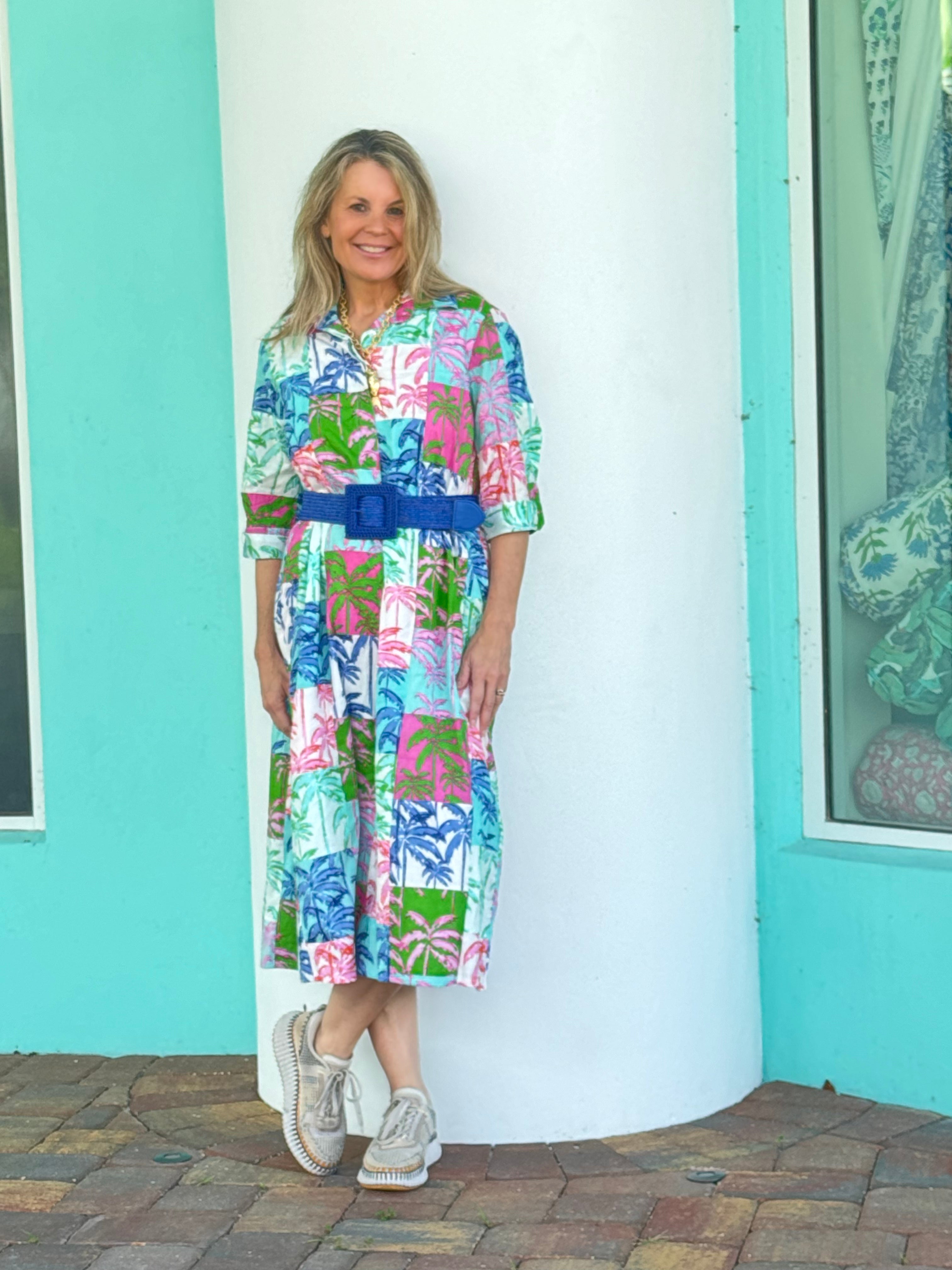 Woman wearing a colorful dress with a blue belt standing in front of a turquoise wall.