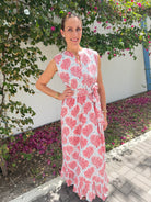Woman wearing a pink and white patterned dress standing in a garden with flowers.